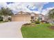 Charming home with manicured front lawn, mature trees, and a two-car garage under a sunny blue sky at 627 Leeds Pl, The Villages, FL 32162