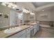 Elegant bathroom with double sinks, granite countertops, stylish lighting, a soaking tub, and a glass block shower at 2204 Baypoint Way, The Villages, FL 32162