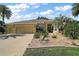 Beautiful home with a three-car garage, tan exterior, desert landscaping, and a brick paved driveway at 2204 Baypoint Way, The Villages, FL 32162