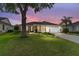 Dusk view of single-story home featuring a two-car garage, manicured lawn and mature trees under a colorful sky at 467 Weston Manor Dr, The Villages, FL 32162