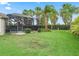 A sprawling backyard featuring lush green grass and a screened-in pool with tropical trees at 631 Independence Path, The Villages, FL 32163