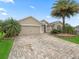 Attractive home with lush landscaping, a brick driveway, and a prominent palm tree at 631 Independence Path, The Villages, FL 32163