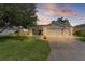 Charming single-story home featuring a well-manicured lawn, mature tree, and attached two-car garage at sunset at 898 Abaco Path, The Villages, FL 32163
