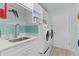 Bright laundry room features modern washer and dryer, utility sink, blue backsplash, and ample storage at 898 Abaco Path, The Villages, FL 32163