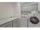 Bright laundry room featuring gray cabinets, white sink, and modern washer and dryer at 11287 Stewart Loop, Oxford, FL 34484