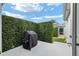 Private patio featuring a grill, tall hedges, and a screened-in lanai entrance under a sunny sky at 1521 Southport St, The Villages, FL 32162