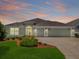 Charming single-story home featuring a manicured lawn, a three-car garage, and an inviting arched entryway with beautiful sunset hues at 2568 Jupiter Way, The Villages, FL 32163