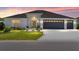Charming home at sunset featuring a well-manicured lawn, a two-car garage, and decorative front door with a wreath at 2988 Sentell St, The Villages, FL 32163