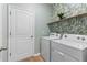 Bright laundry room with white washer and dryer, shelf, and decorative palm leaf wallpaper at 3060 Neverland Dr, New Smyrna Beach, FL 32168
