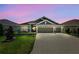 Charming single-story home with well-manicured lawn, three car garage, and neutral palette under a dramatic pink and purple sky at 6243 Danielson Loop, The Villages, FL 32163