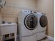 Laundry room with white washer and dryer, utility sink, wire rack shelving, and dark vinyl floor at 10994 Se 168Th Loop, Summerfield, FL 34491
