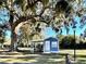 Charming blue house featuring a covered parking area under a big tree with hanging Spanish moss in a sunny park setting at 12077 Lakeshore Way, Oxford, FL 34484