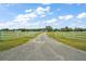 Gated driveway leads to a charming home with a white fence and lush green fields, offering privacy and space at 1560 Ne 17Th St, Sumterville, FL 33585