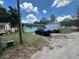 Exterior view of the single-story home with an overgrown yard, featuring a green exterior and a black vehicle at 102 Harold St, Leesburg, FL 34748
