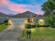 Inviting home exterior featuring a well-lit garage, landscaped yard, and charming front entrance under a colorful sky at 10986 Se 171St Street Rd, Summerfield, FL 34491