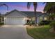 Charming single-story home featuring an attached two-car garage and lush landscaping with mature palm trees at dusk at 762 Turbeville Ter, The Villages, FL 32162