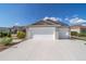 A light brown home featuring a spacious driveway and a two-car garage on a sunny day at 997 Nash Loop, The Villages, FL 32162