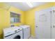 A yellow laundry room is equipped with a washer and dryer, as well as a white door at 1910 Quiet Oak Ct, The Villages, FL 32162