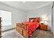 Bright bedroom featuring a wooden bed frame with red bedding, a bedside table, and a window for natural light at 33960 Sky Blossom Cir, Leesburg, FL 34788