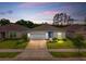 Dusk shot of a well-lit, single-story home with a manicured front lawn, highlighting its inviting curb appeal at 33960 Sky Blossom Cir, Leesburg, FL 34788