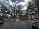 Exterior view of parking lot with mature trees and building in the background under a cloudy sky at 5560 Metrowest Blvd # 3-204, Orlando, FL 32811