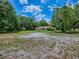 Wide shot of the home with a red roof surrounded by a large grassy yard and leafy trees at 9144 Sw 156Th Pl, Dunnellon, FL 34432
