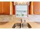 Close-up of a kitchen sink with a garden view through the window and wood cabinets at 1282 Fort Lawn Loop, The Villages, FL 32162