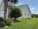 Landscaped side yard featuring a well-maintained lawn, mature trees, and colorful flower beds at 1512 Nueva Pl, The Villages, FL 32159