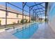 Long, screened-in pool with clear water and a travertine tile deck with view of house at 2077 Vickers Pl, The Villages, FL 32163