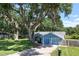 View of the home with mature trees, blue paint, and a two-car garage at 5380 County Road 122, Wildwood, FL 34785