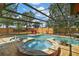 Screened-in pool and hot tub area surrounded by a stone patio, lounge chairs, and landscaping at 707 S Dixie Dr, Howey In The Hills, FL 34737