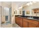 Bathroom featuring dual sinks with a dark countertop, wood cabinets, and a walk-in shower with glass blocks at 1376 Birdsong Pl, The Villages, FL 32163
