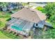 Aerial view of a screened in pool with turquoise water, lush green lawn, and a house with a brown roof at 34231 Shadewood Cir, Leesburg, FL 34788