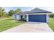 Charming single-story home featuring a blue garage door, grey roof, nicely landscaped front yard, and long driveway at 472 Malauka Radl, Ocklawaha, FL 32179