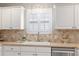 Well-lit kitchen sink area with tiled backsplash, white cabinets, and a view from the window at 579 Audrey Ln, The Villages, FL 32162