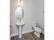 Modern powder room featuring a pedestal sink, oval mirror, and wood-look flooring at 10302 Pearson Ave, Orlando, FL 32827