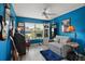 The room features bright blue walls, a ceiling fan, and a gray loveseat for comfort at 2448 Bachman Path, The Villages, FL 32162