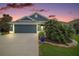 Charming single-story home featuring a well-manicured lawn, a two-car garage, and a beautifully landscaped yard at dusk at 2448 Bachman Path, The Villages, FL 32162