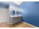 Well-lit bathroom with tiled floors, double sinks, two circular mirrors, blue walls, and a cabinet for storage at 800 Daybreak Dr, Fruitland Park, FL 34731