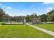 A fenced playground with swings and colorful play structures sits on a lush green lawn under a bright blue sky at 800 Daybreak Dr, Fruitland Park, FL 34731