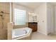 Bright bathroom showcasing a soaking tub, tiled shower, glass block window, and vanity with dark countertop at 29152 David Ct, Tavares, FL 32778