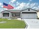 Charming single-story home with a well-manicured lawn, brick accents, and a large American flag in the front yard at 3237 Atwell Ave, The Villages, FL 32162