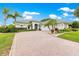 Inviting white facade with well-kept shrubs and palm trees, leading to a brick paved drive and a multi-car garage at 39145 Treeline Dr, Lady Lake, FL 32159