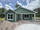 Charming green home with white trim, a cozy porch, and bright windows, set against a backdrop of blue skies and scattered clouds at 891 Cr 482C, Lake Panasoffkee, FL 33538