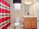 Well-lit bathroom featuring a shower with red curtain, toilet, and vanity with mirror at 9335 San Jose Blvd, Howey In The Hills, FL 34737
