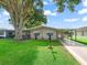 Charming single-story home featuring a covered carport, a well-manicured lawn, and mature trees providing ample shade at 1005 Richard Dr, The Villages, FL 32159