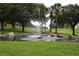 Scenic pond with a fountain, surrounded by mature trees and well-maintained landscaping at 1355 Misty Glen Ln, Clermont, FL 34711