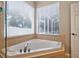 Bright bathroom featuring corner tub with tan tile surround under two windows with closed blinds at 33316 Irongate Dr, Leesburg, FL 34748