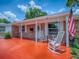 Quaint home exterior showcases a brick facade, rocking chairs on the porch, and a vibrant orange entryway at 564 Lancaster Ave, Orange City, FL 32763