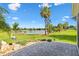 Beautiful backyard with a brick patio, mature palm trees, and stunning lake views beyond the green lawn at 5746 Botner Dr, The Villages, FL 32163